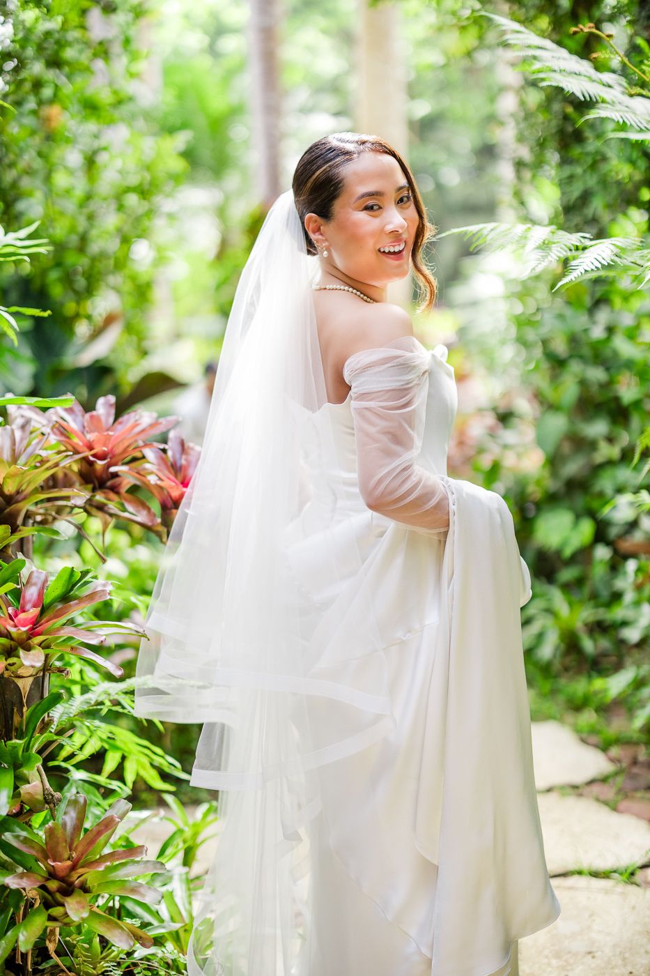 Joyful bridal portraits with flowing veil against green garden foliage.
