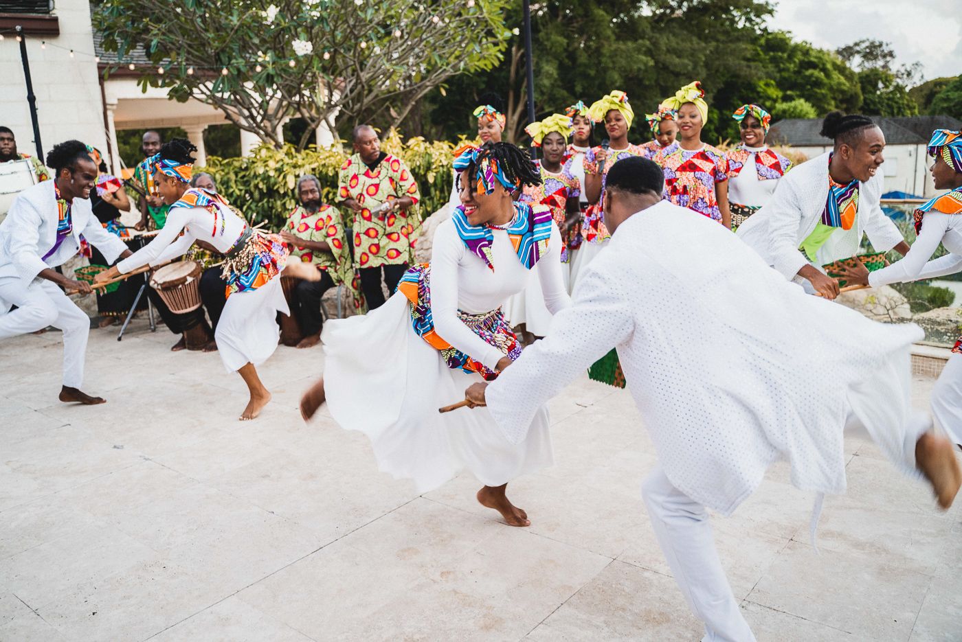 Group of wedding guests performing synchronized dance moves in white attire on outdoor patio.