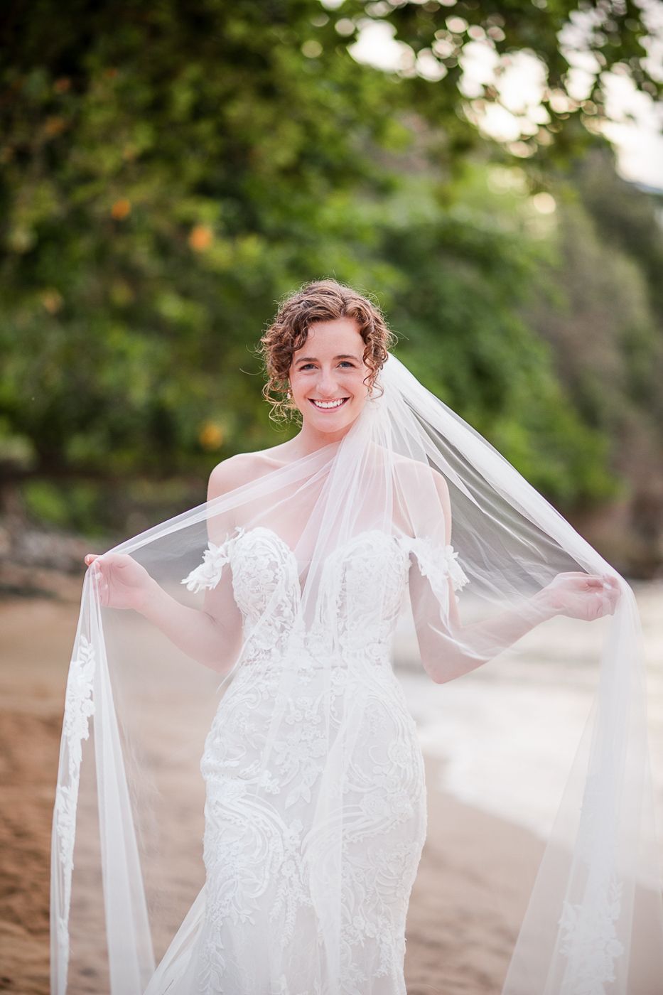 A wedding dress with intricate lace details and flowing veil photographed outdoors.