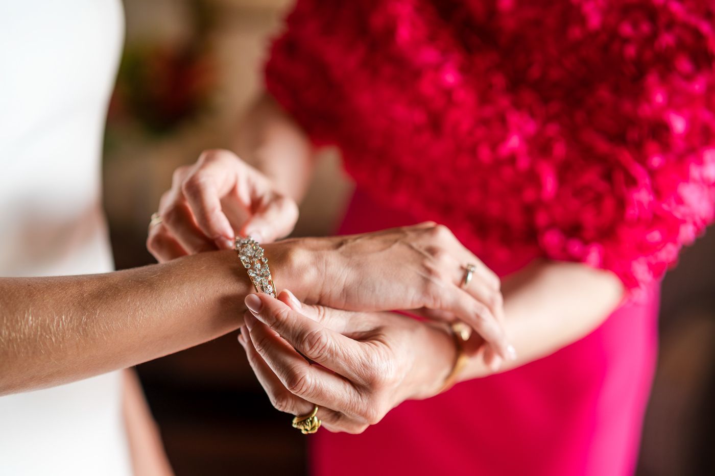 Hands fastening jewelry while wearing a bright red formal dress.