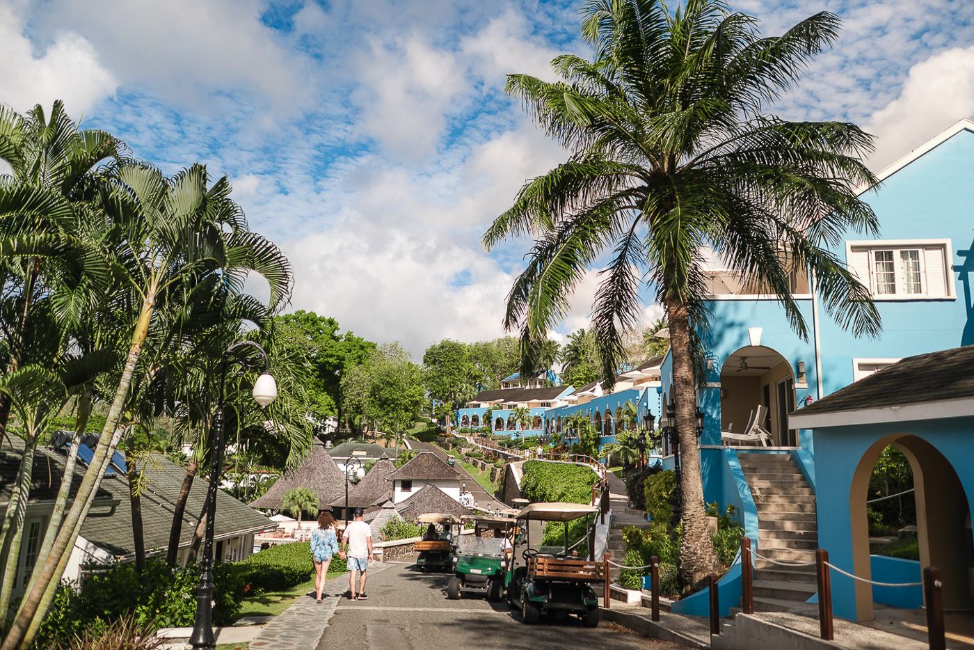 A vibrant Caribbean street scene with palm trees, blue buildings and beach umbrellas.