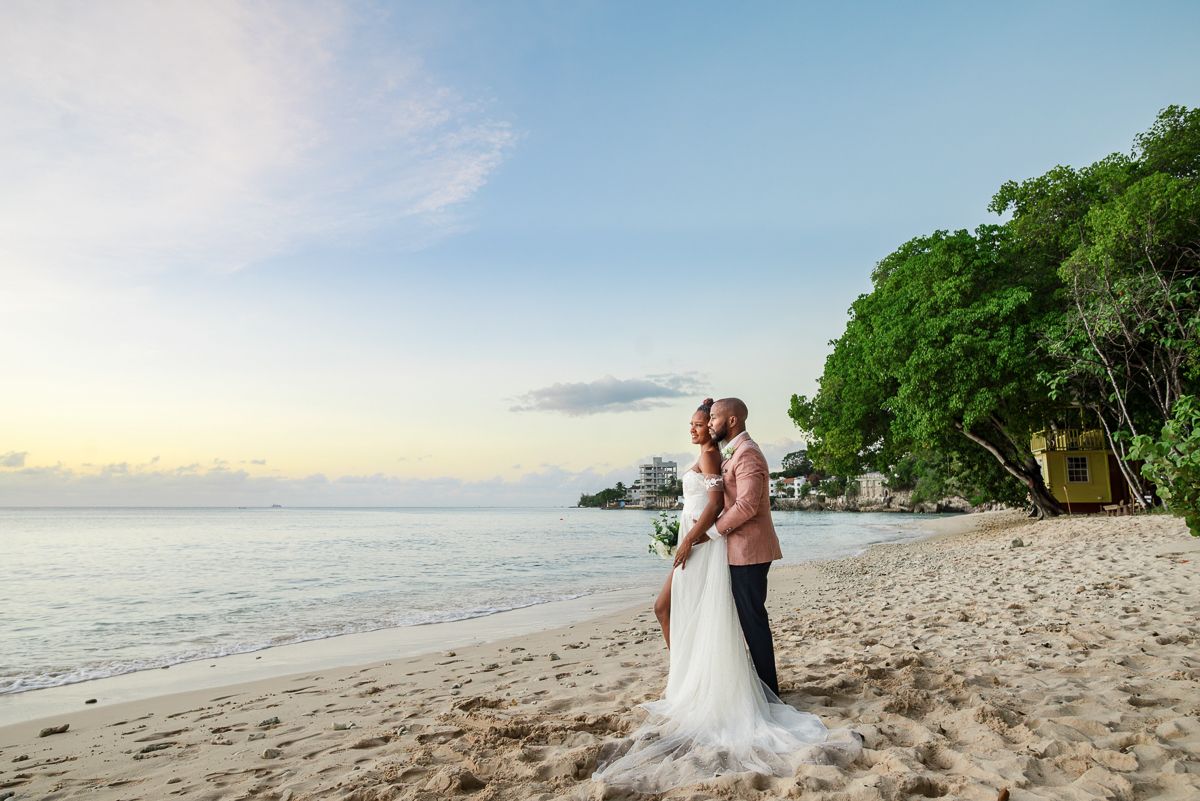 Romantic beach wedding photoshoot at sunset with waves crashing on tropical shoreline.