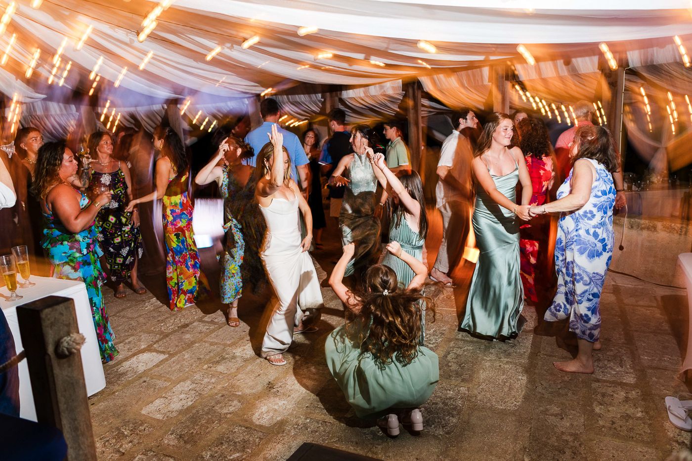 Guests dancing joyfully at an outdoor wedding reception under string lights and draped fabric canopy.