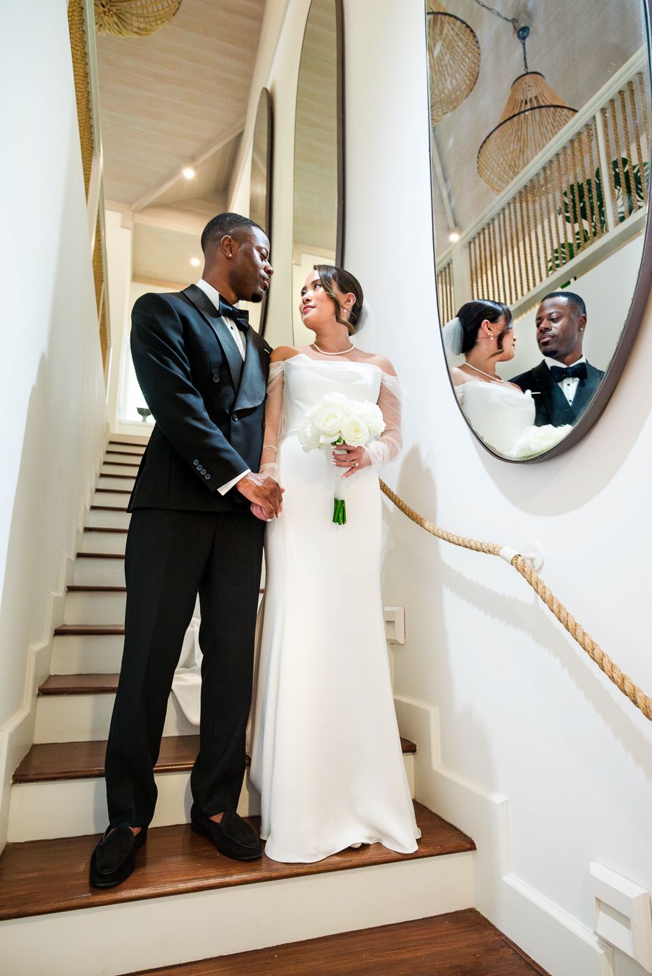 Wedding couple shares an intimate moment on an elegant staircase with a mirror reflection in a bright interior setting.