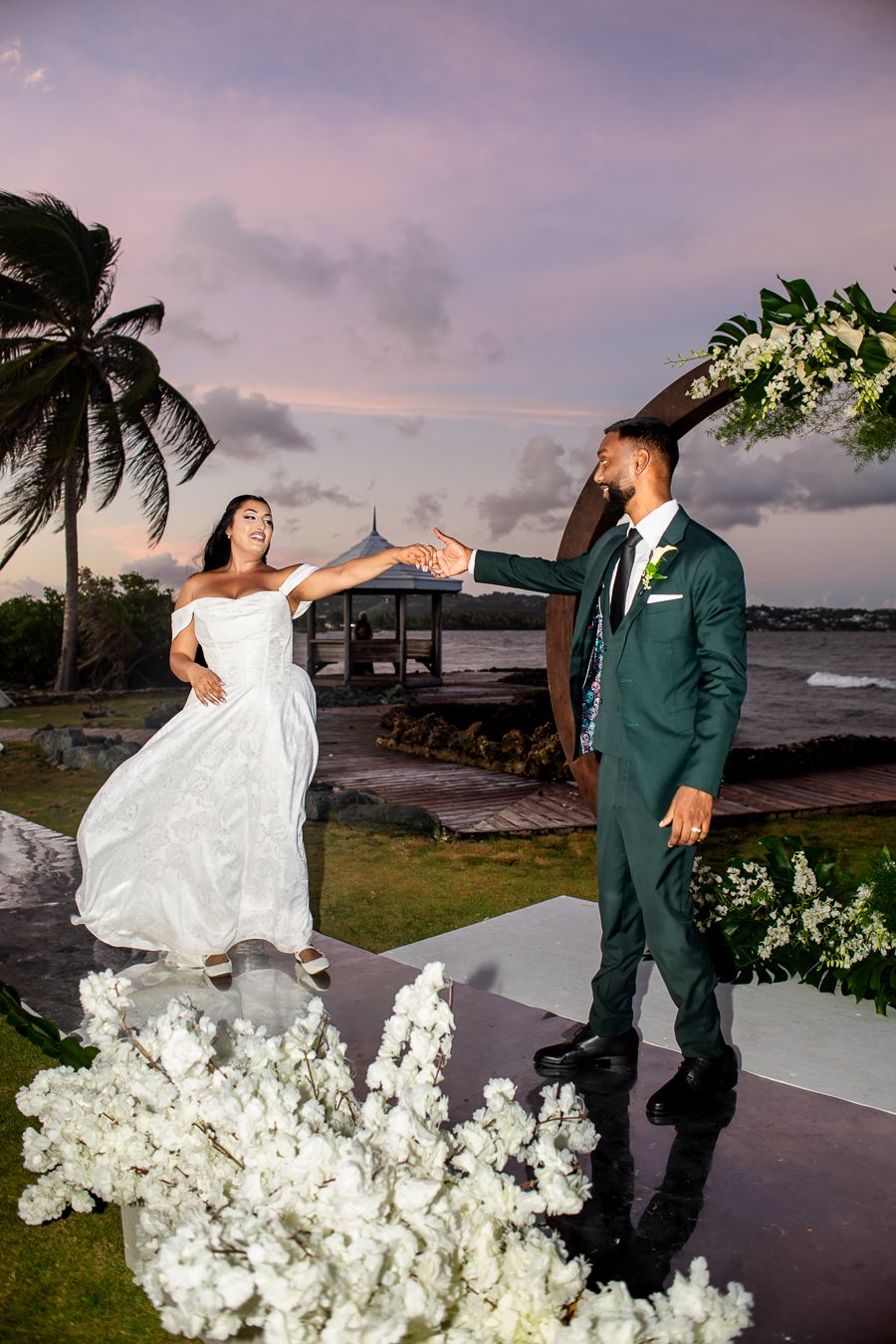 Romantic wedding photoshoot on a beachside path with flowing white dress and tropical landscaping.