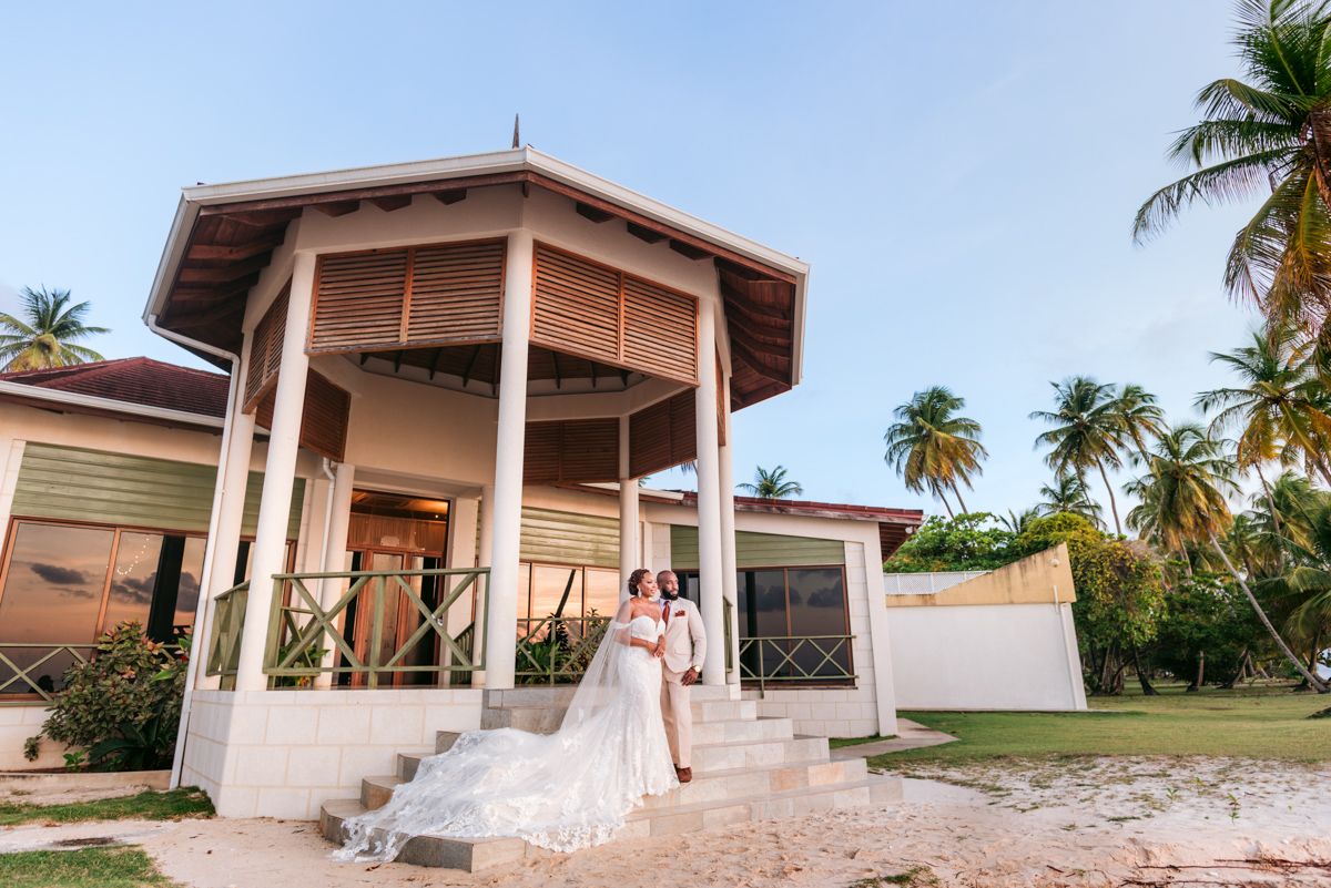 Bride poses in flowing white dress at sunset in front of tropical beach house with gazebo.