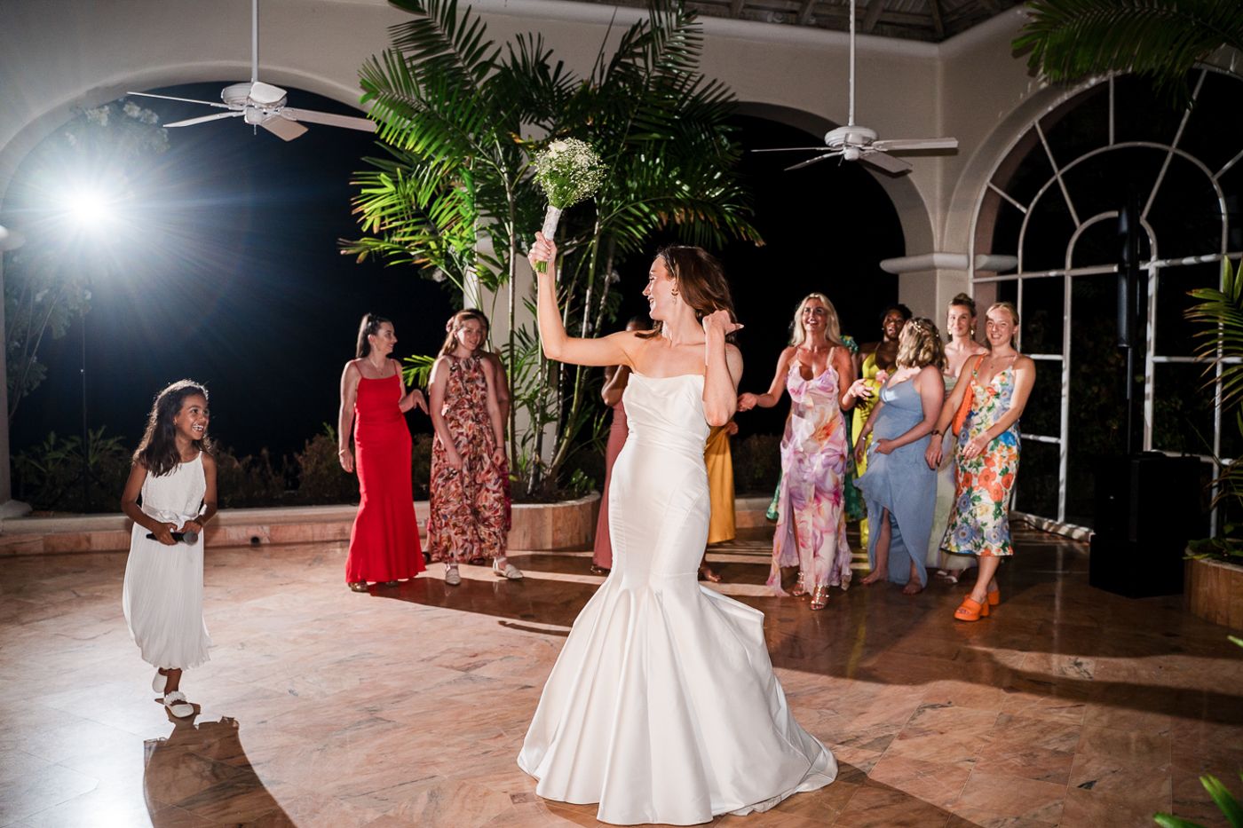 A wedding bouquet toss moment in an indoor venue with elegant arches and tropical decor.