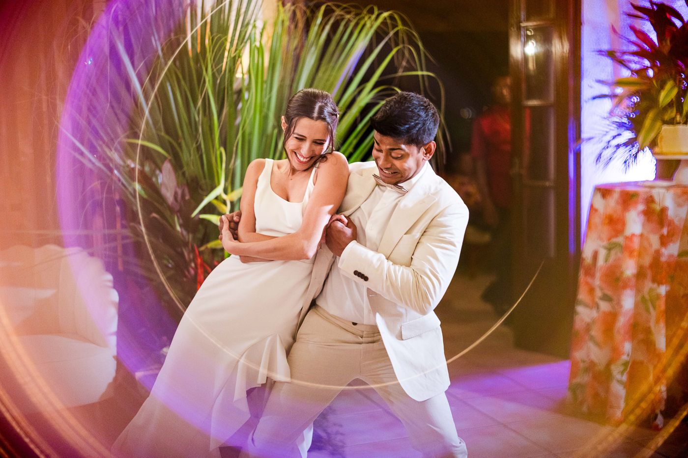 Dancing couple performs dramatic moves in front of tropical plants with purple lighting.