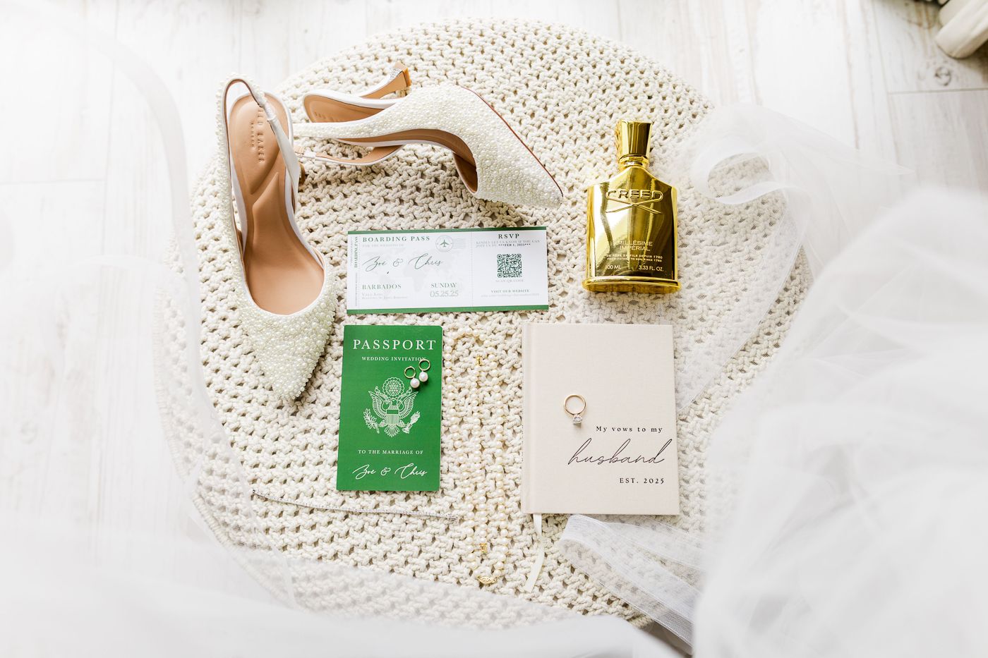 Wedding details flatlay with high heels, perfume bottle, and invitation on white knit background.
