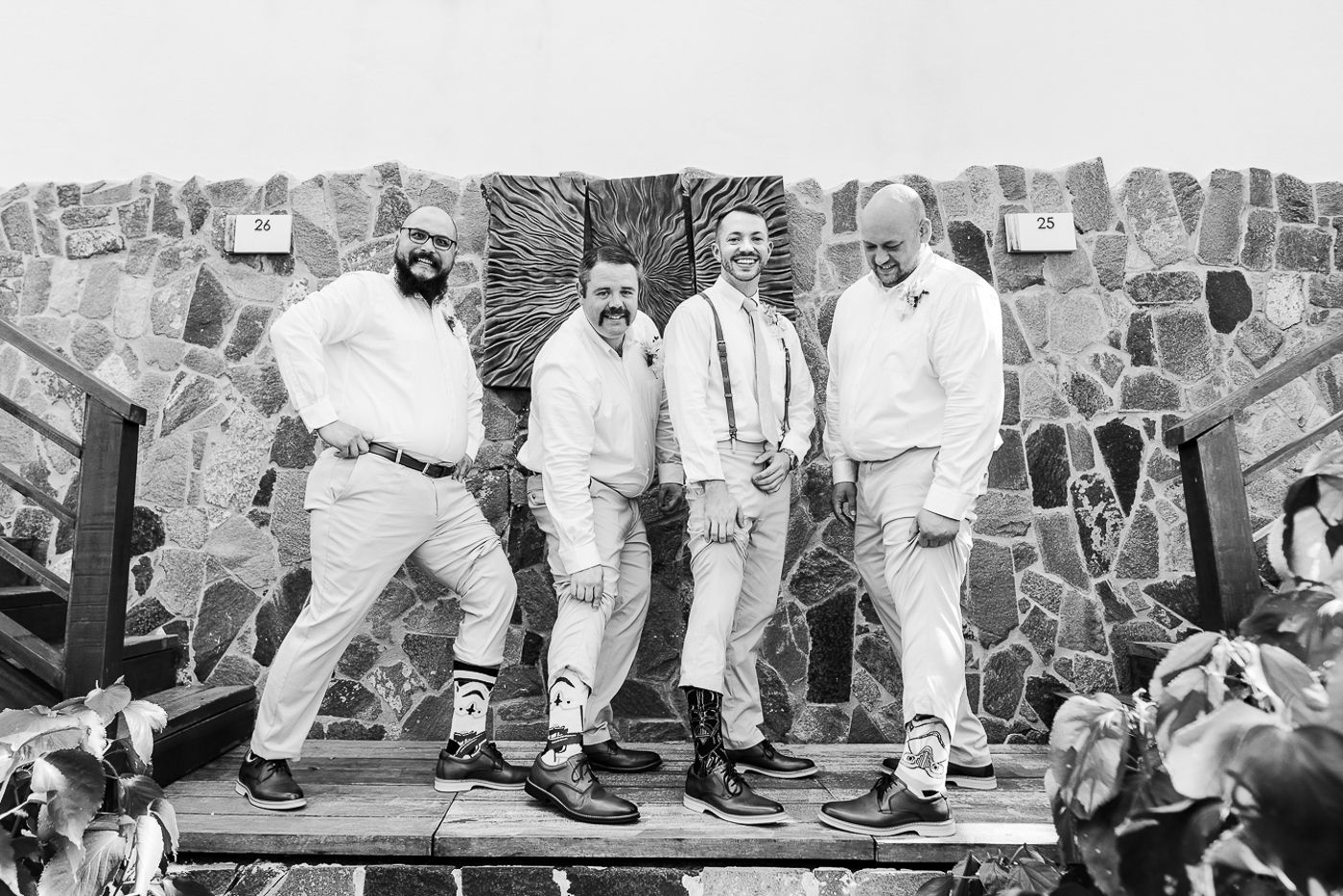 Black and white photo of group posing playfully against stone wall wearing coordinated outfits.