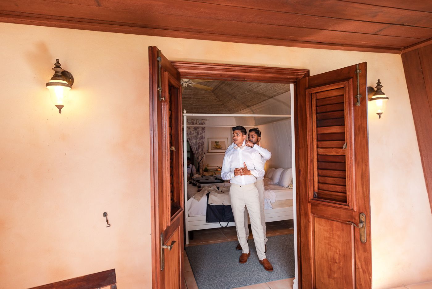 Someone in all white attire stands in a doorway of a rustic room with wooden doors.