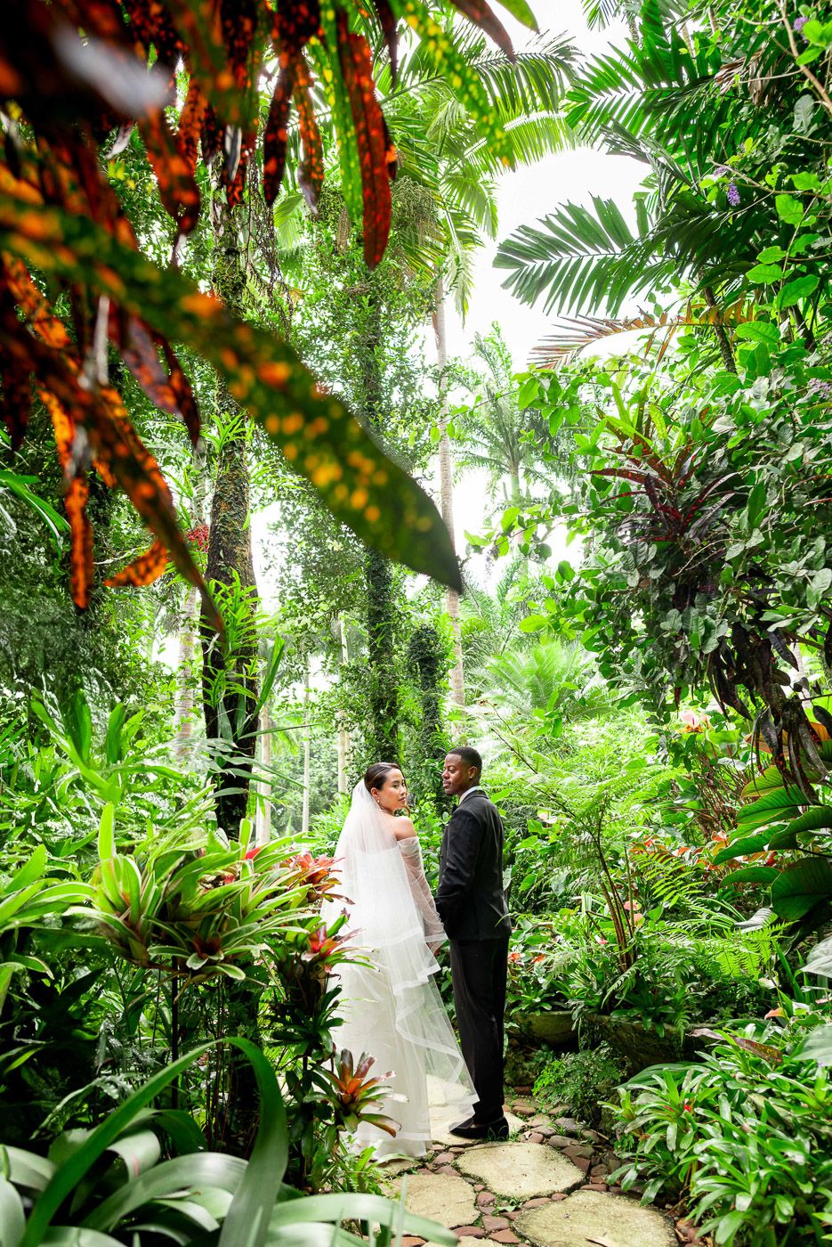 Dreamy wedding ceremony captured in a tropical garden with vibrant red florals and lush greenery.