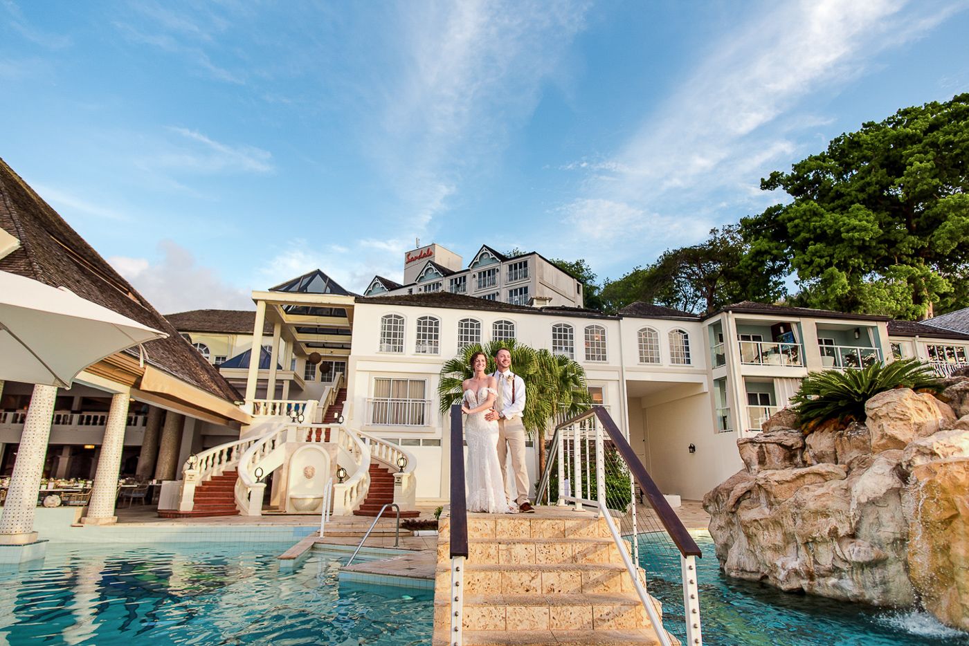 Luxury waterfront wedding venue with grand white mansion and swimming pool under blue skies.