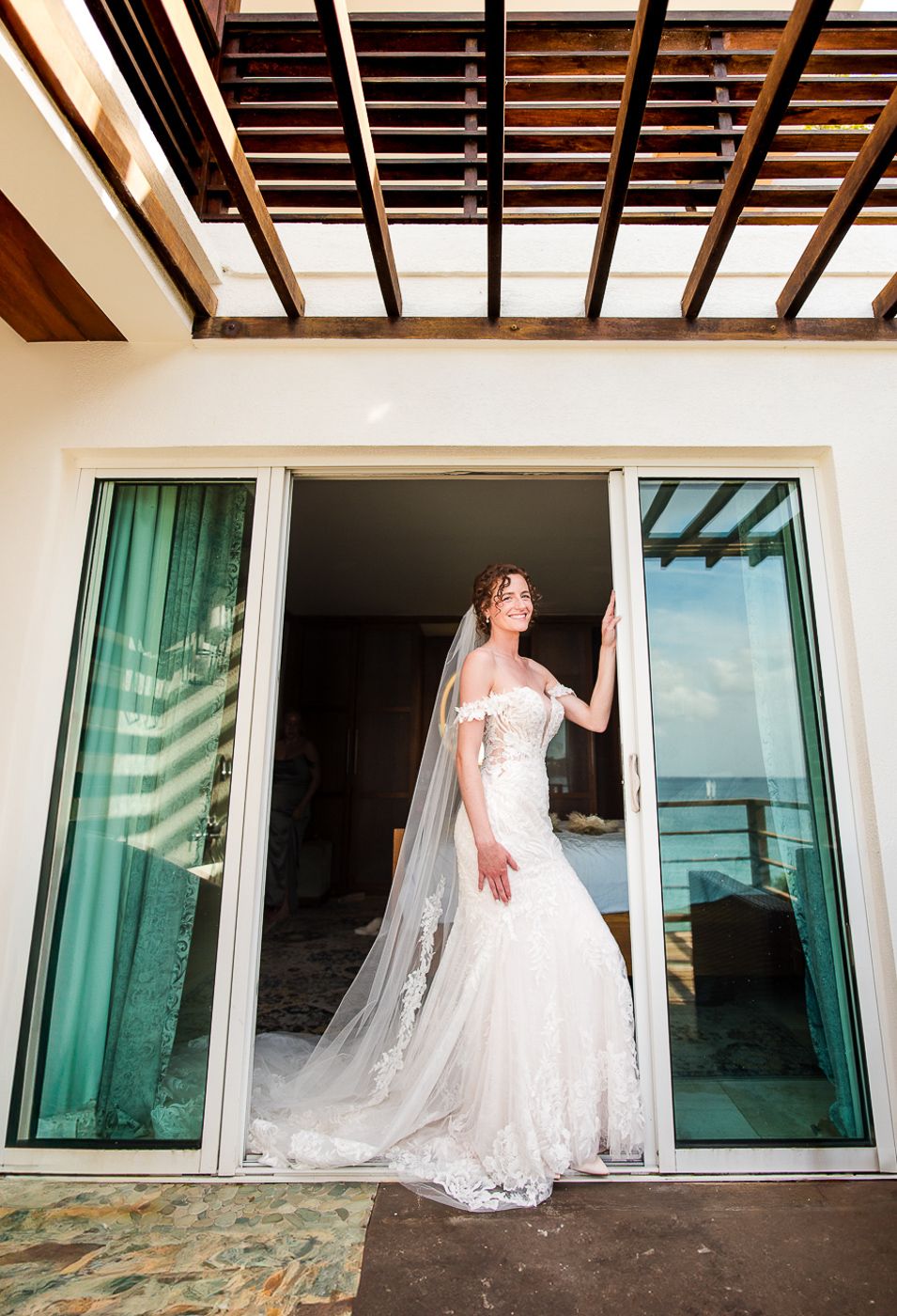 Wedding dress with cathedral veil captured against modern sliding glass doors and wooden beams.