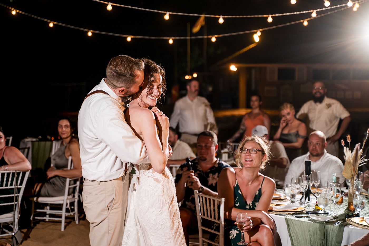 Wedding reception party with string lights and guests dancing on the beach.