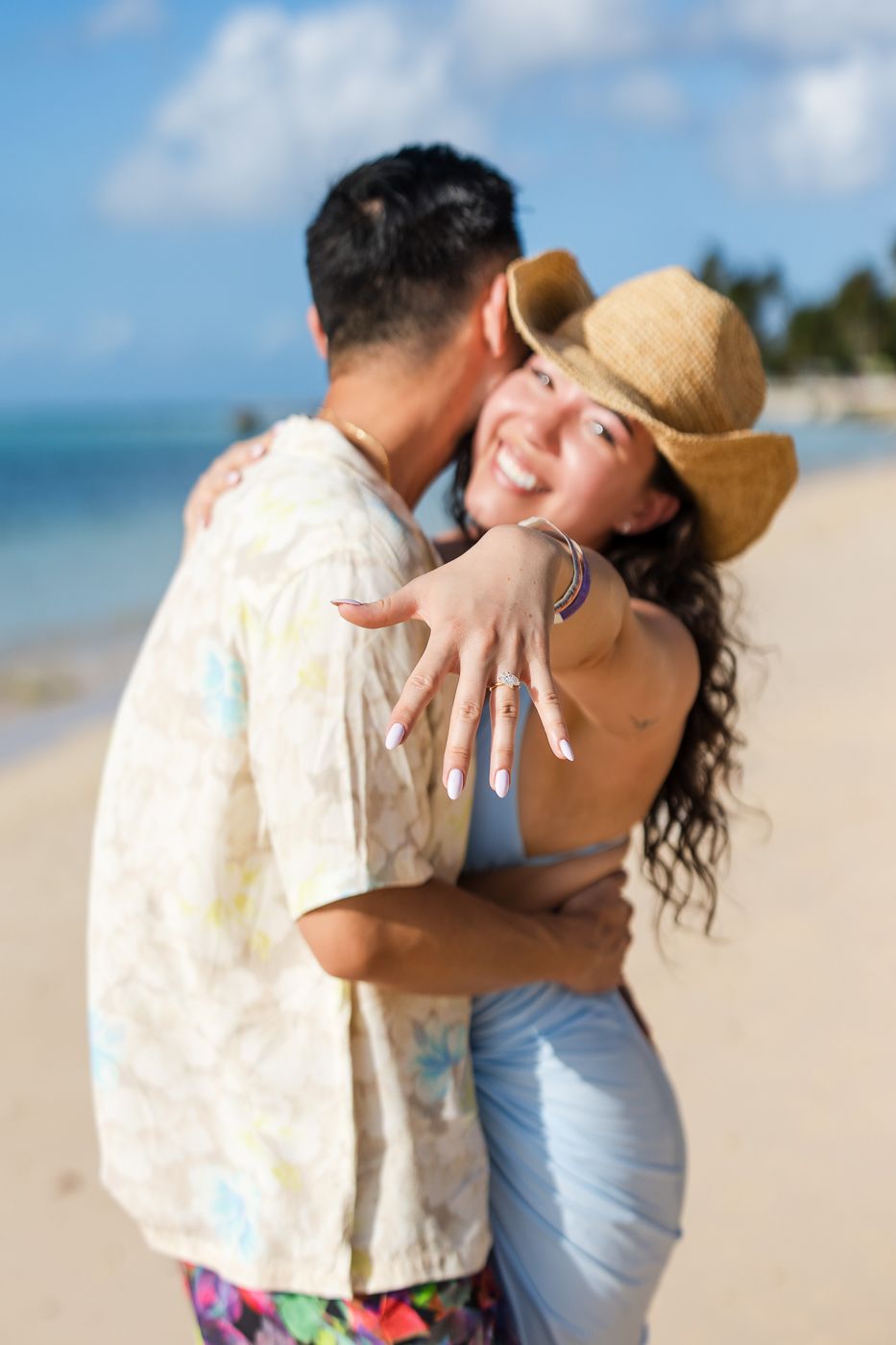 Romantic beach proposal moment with sparkling ocean and palm trees in background.