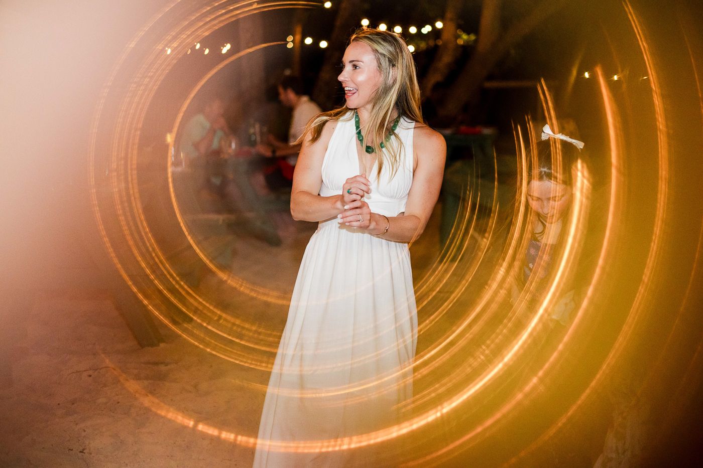 Woman in white dress dancing with golden light trails swirling around her at an elegant evening event.
