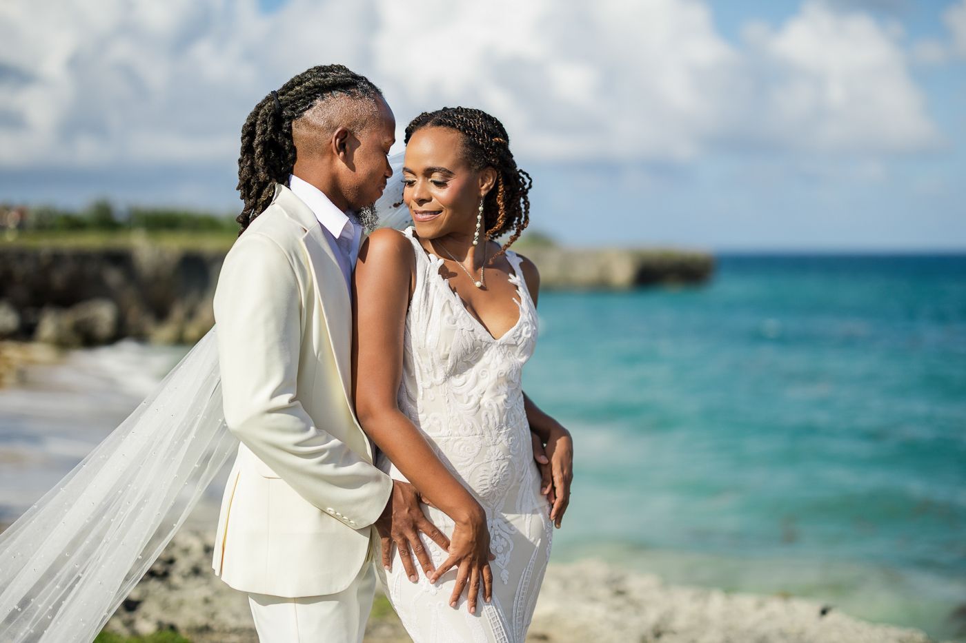 A happy couple shares intimate moments on a beautiful beach with turquoise waters and white sand in the background.