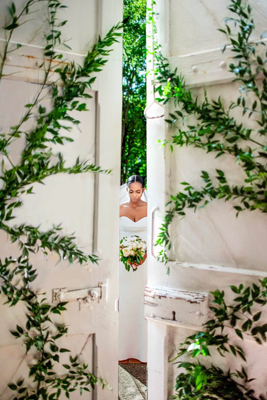 Creative wedding photo through greenery and white architectural elements creating a framed view.