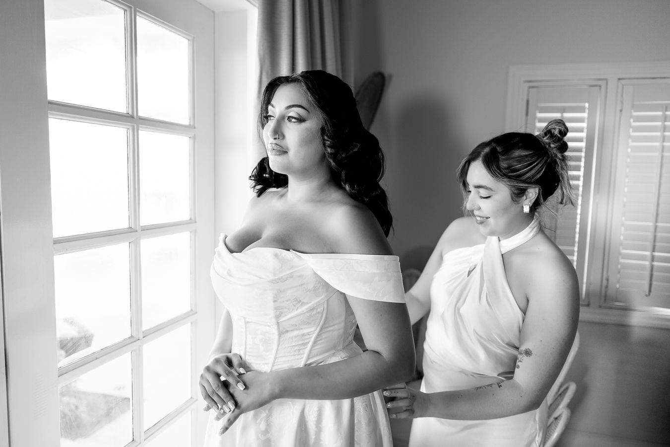Black and white photo capturing candid wedding moments in a bright interior setting.