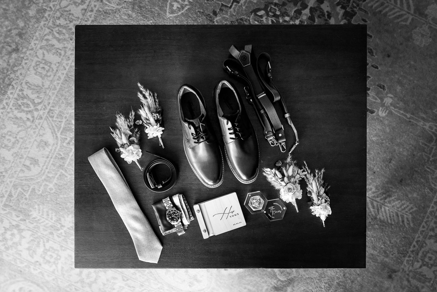 Wedding accessories including rings and shoes arranged artistically in monochrome.