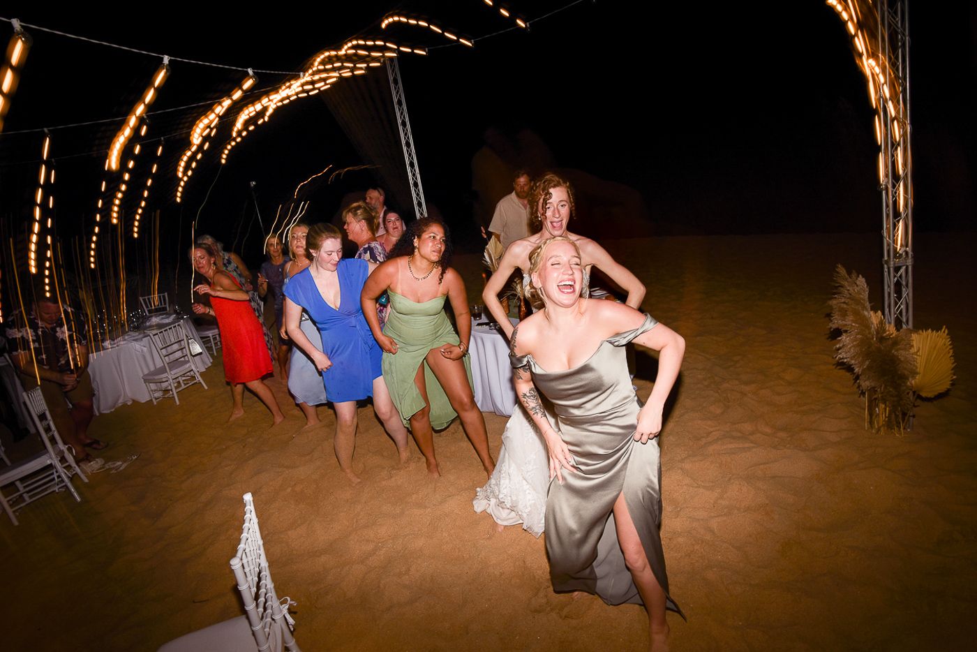 Wedding guests dance and celebrate on the beach under the night sky.