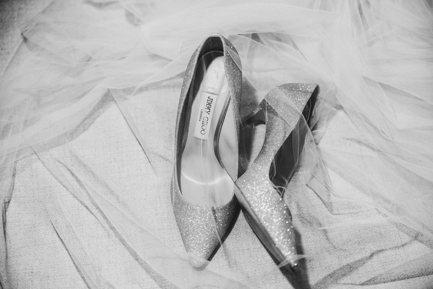 Elegant white satin wedding shoes with delicate straps and heels arranged on white fabric.