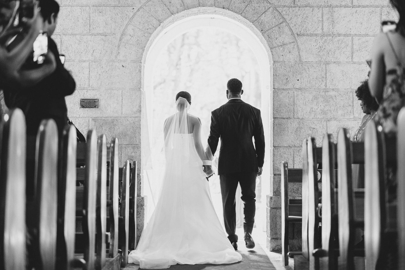 Wedding couple walking through arched stone corridor in black and white photography.