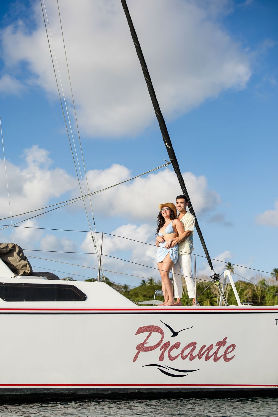 White sailboat named Picante against blue sky with passengers on deck.