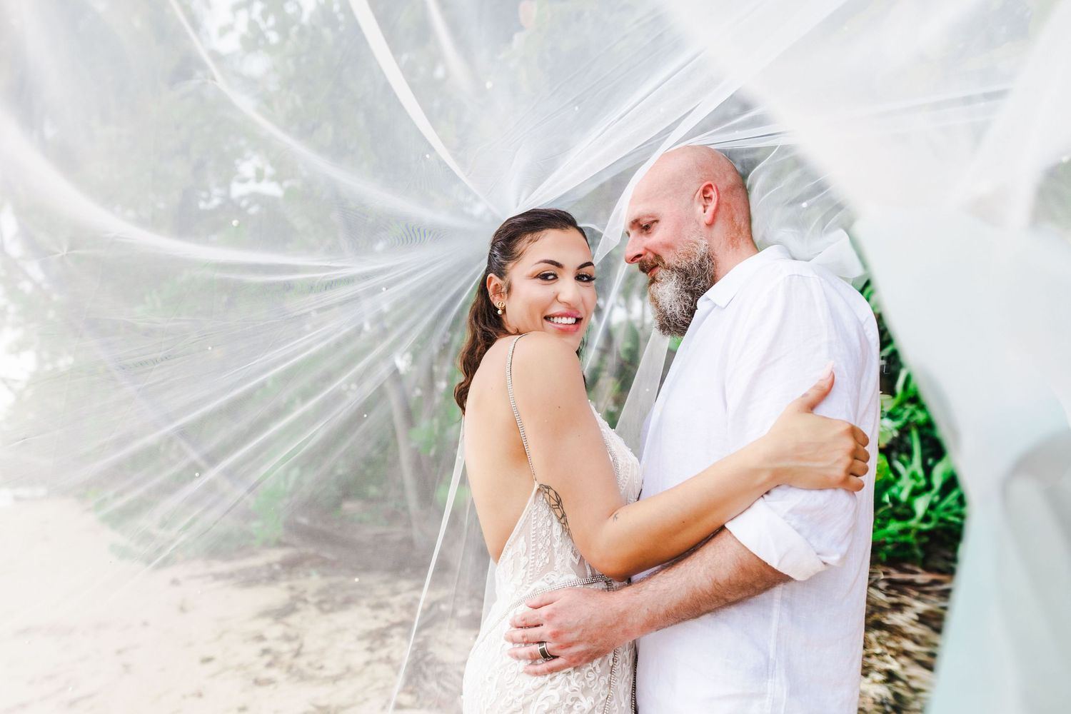 Romantic wedding photos with flowing white veil against a tropical background.