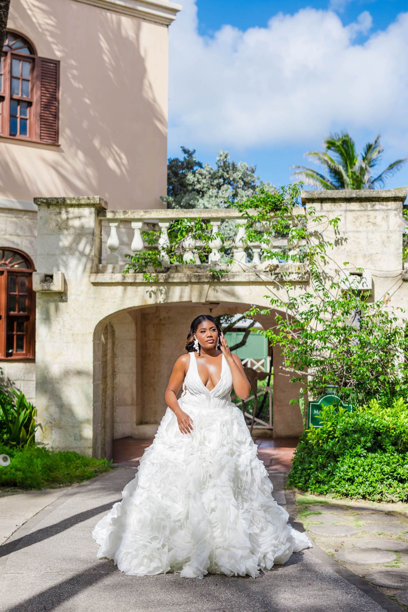 Bride in flowing white dress poses against tropical courtyard architecture.
