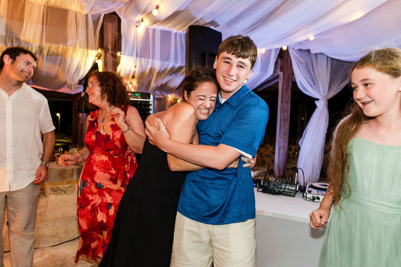 Guests dancing and hugging joyfully at an elegant outdoor wedding reception under a draped tent.