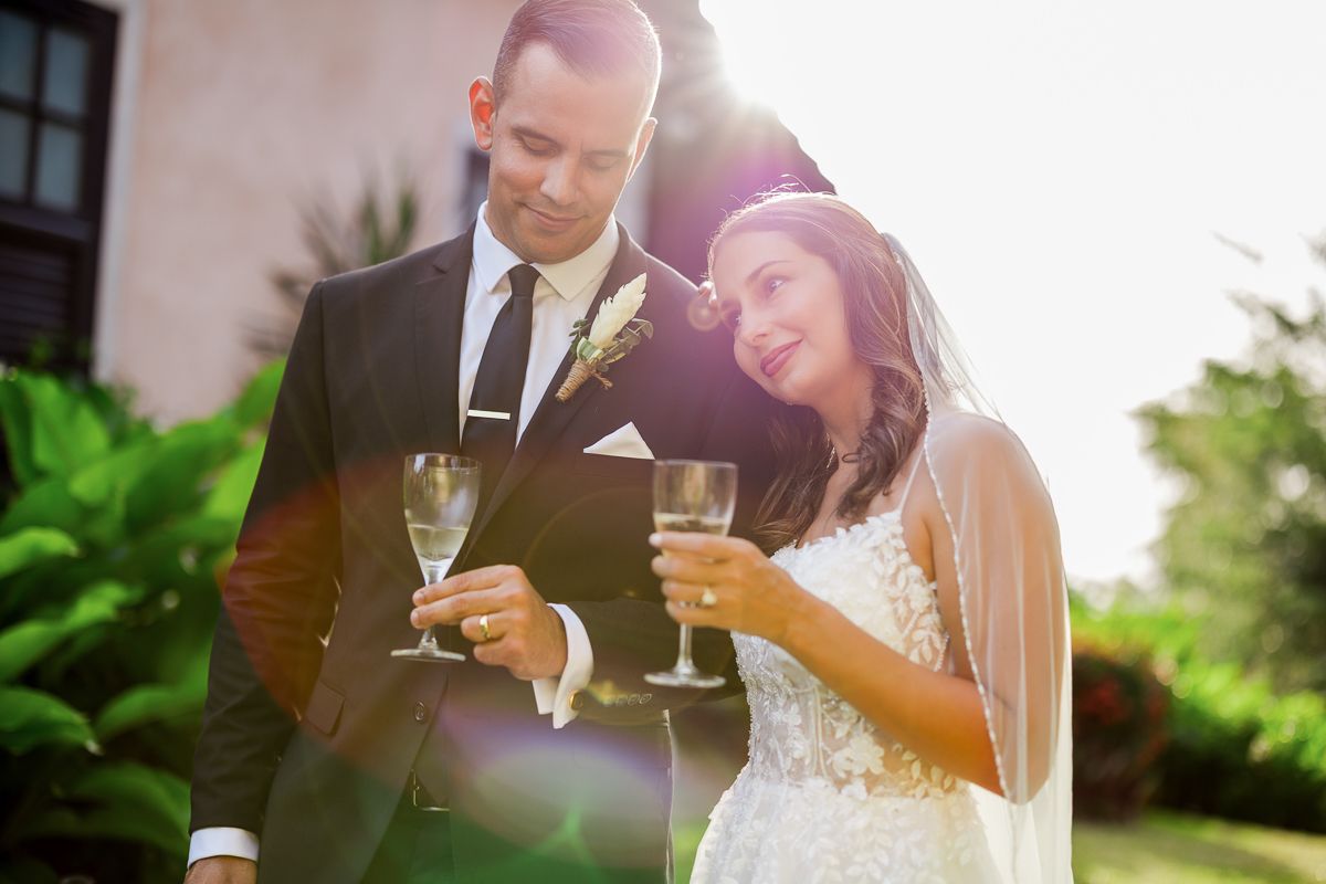 Bride and groom toast with champagne glasses outdoors in golden sunlight on their wedding day.