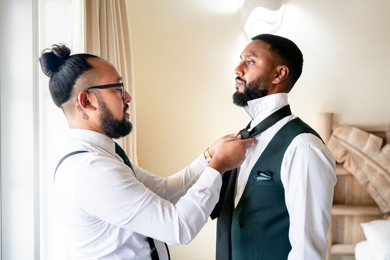 Groomsmen helping each other get ready in a bright room with white walls.