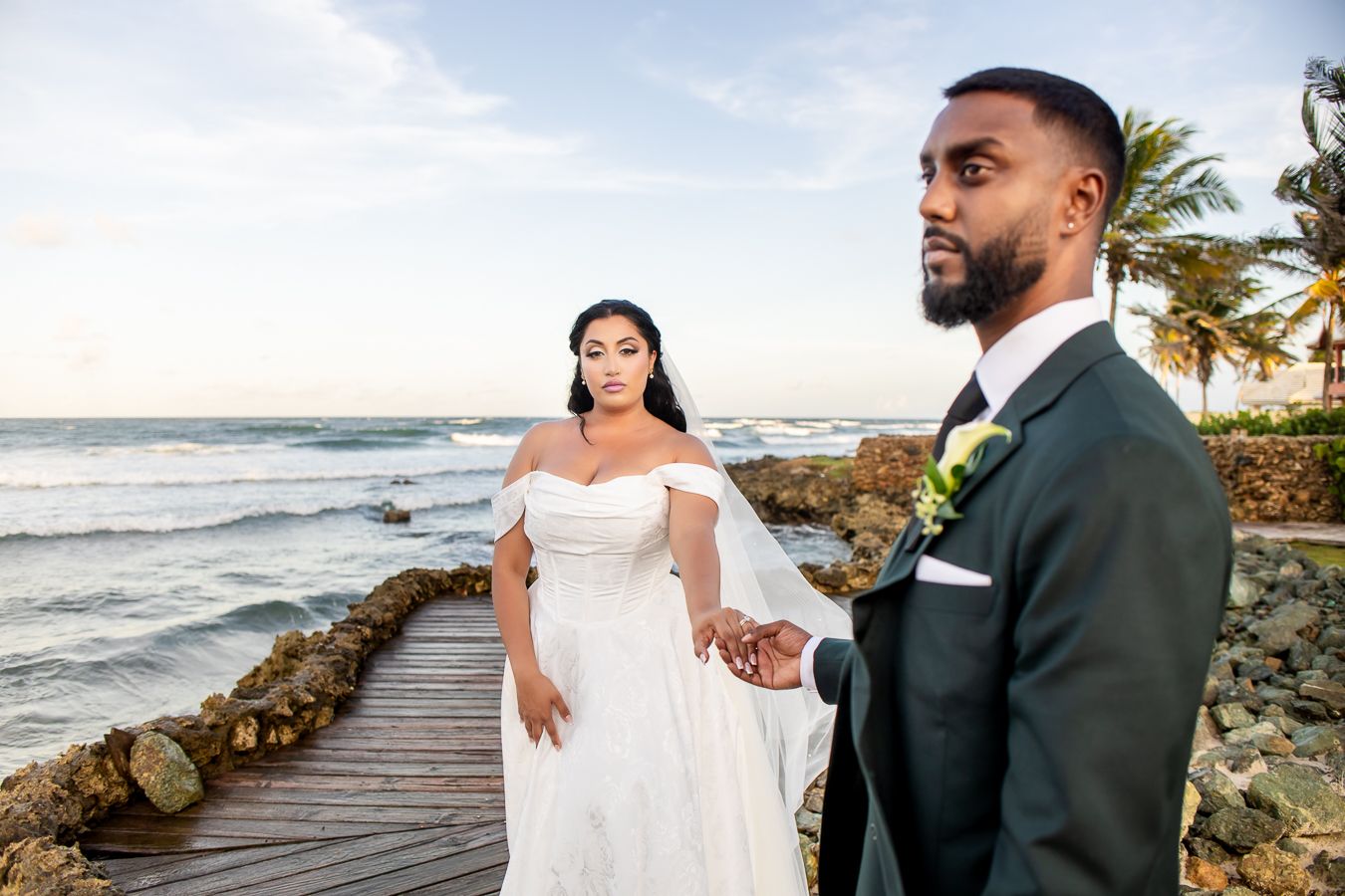Newlyweds share romantic moments along a tropical beach boardwalk at sunset.
