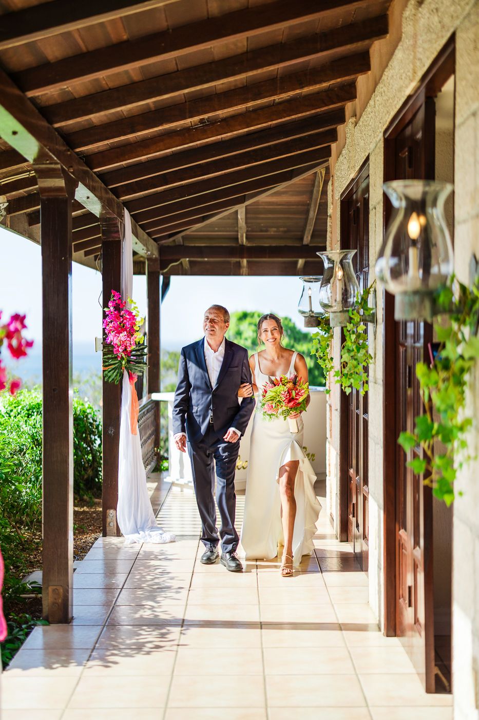 A couple walks down a covered outdoor walkway decorated for a wedding ceremony.