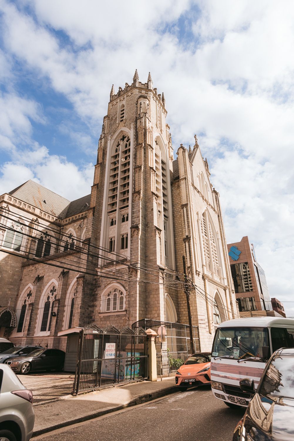 A Gothic cathedral with tall spires and ornate architecture stands on an urban street with parked cars in Brooklyn.