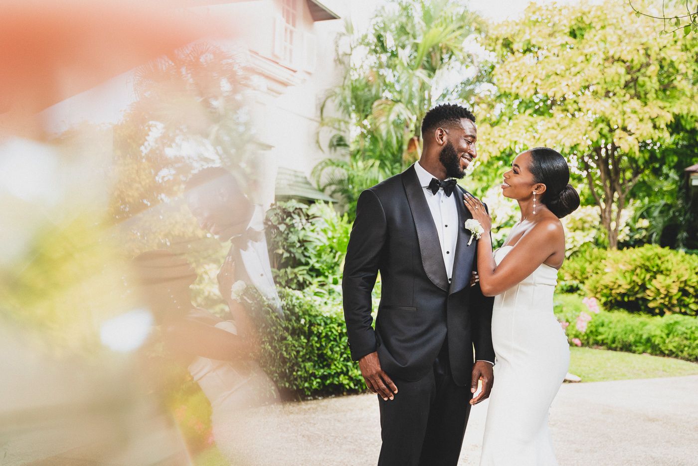 Newlyweds share a romantic moment in a sun-dappled tropical garden setting.