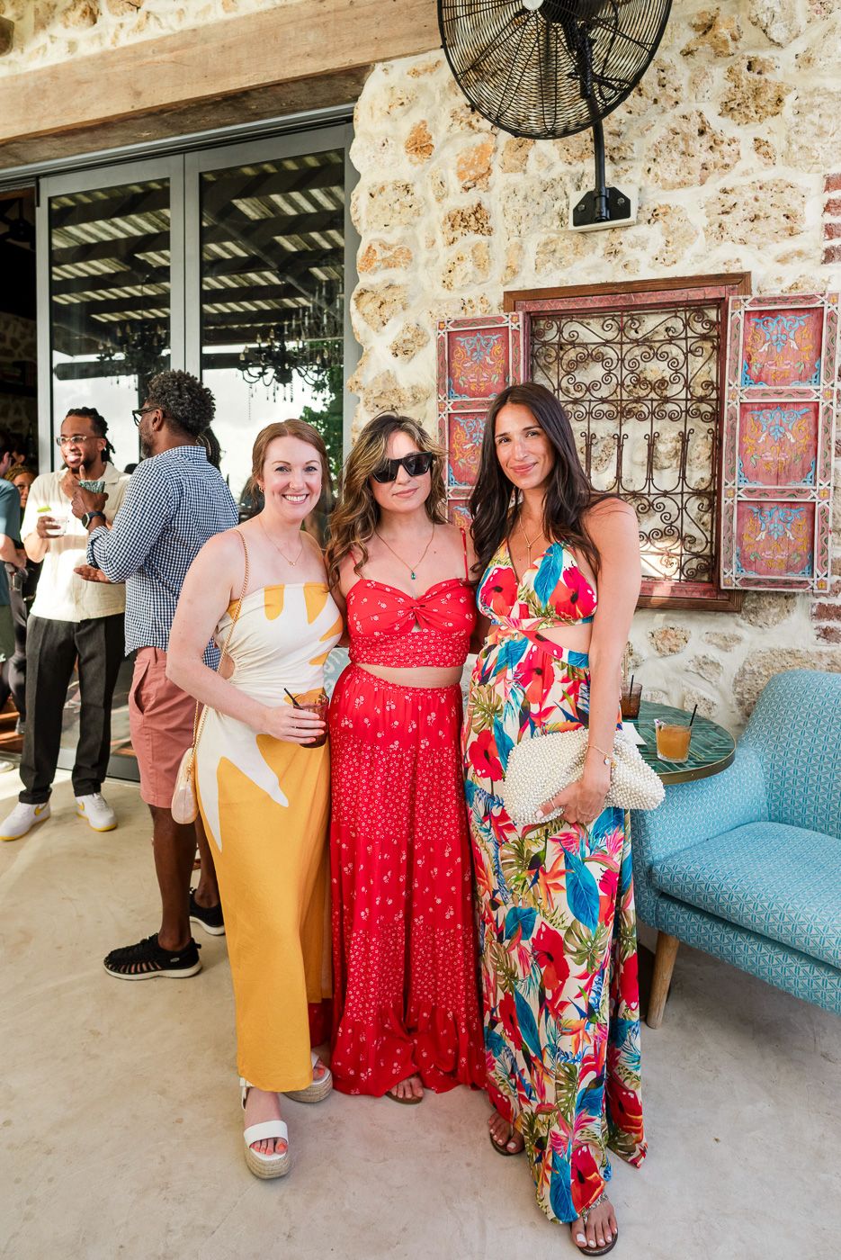 Summer party guests gathering in a rustic stone venue wearing colorful dresses and casual attire.