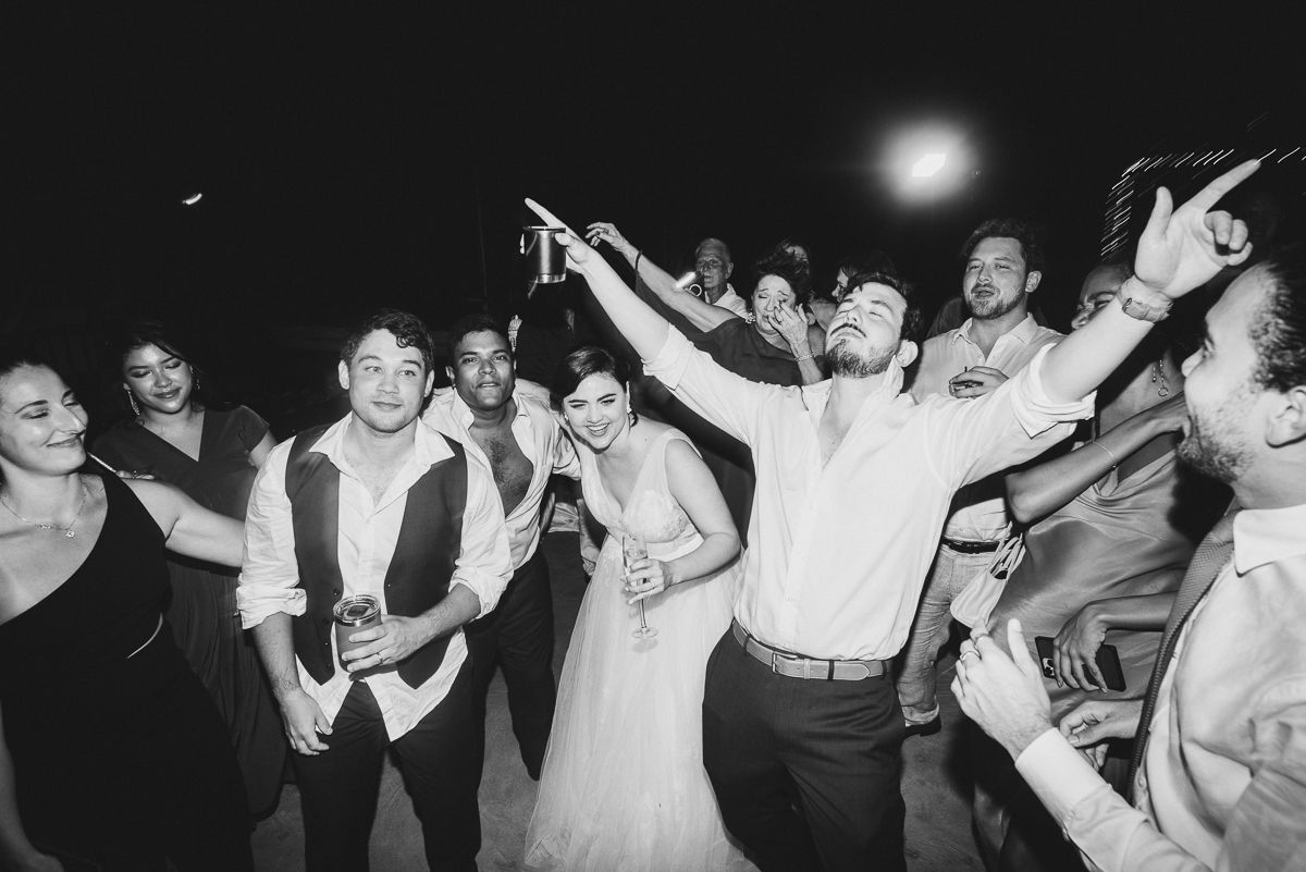 Bride and groom celebrate joyfully with guests on dance floor at lively black and white wedding reception.