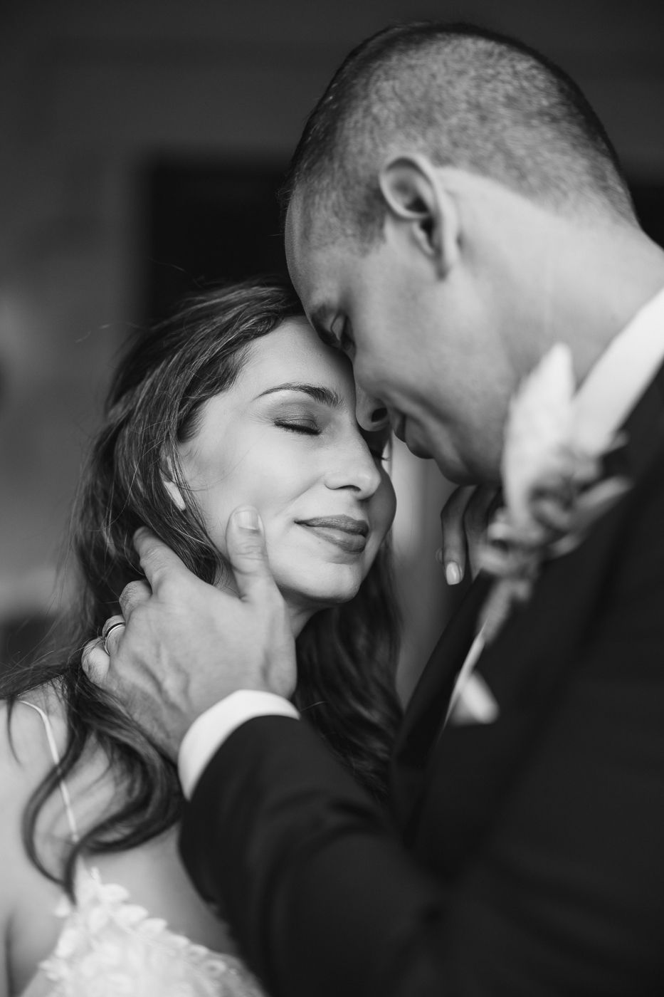 Intimate black and white wedding portrait of bride and groom touching foreheads, groom cradling brides face tenderly.