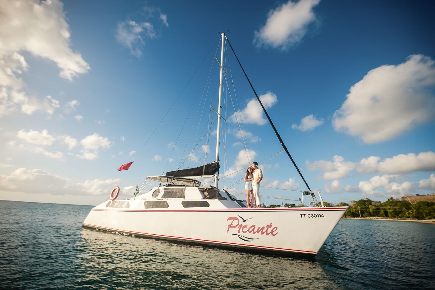 White sailing catamaran anchored in calm tropical waters under blue sky with puffy clouds.