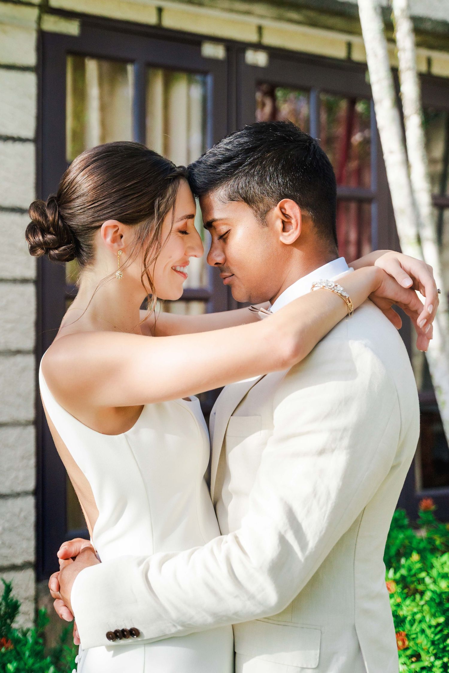 Intimate wedding portraits in matching white outfits against architectural backdrop.