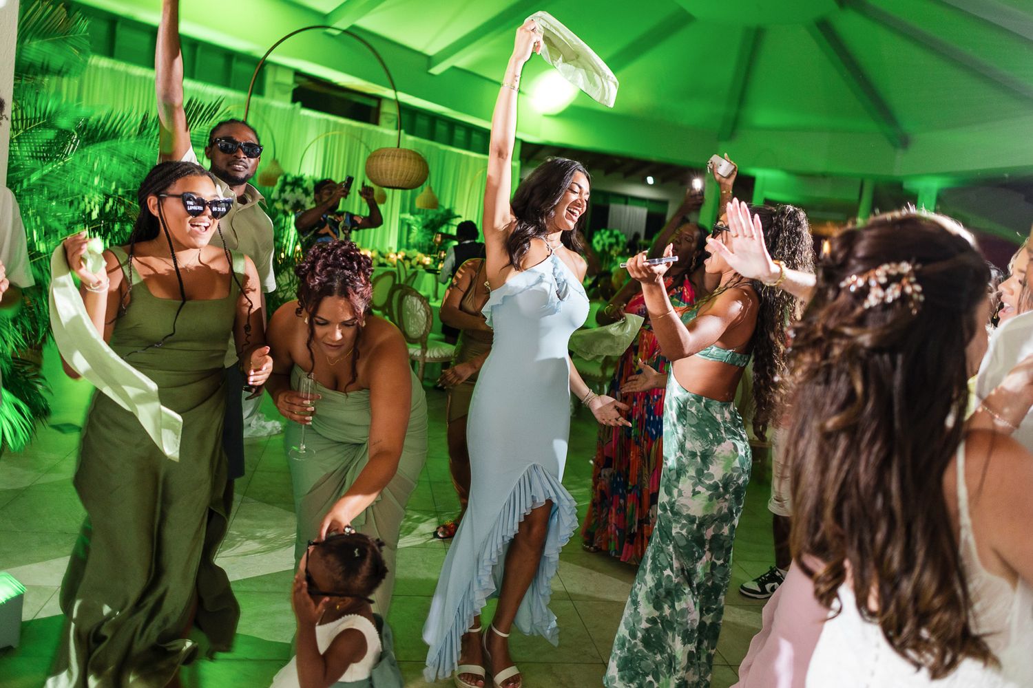 Wedding guests dance and celebrate on a dance floor illuminated with vibrant green lighting at an evening reception.