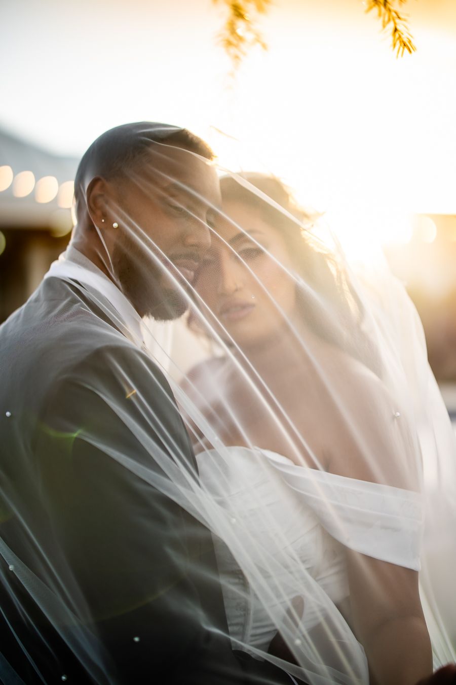 Golden sunlit wedding portraits showcase tender moments between newlyweds through a sheer veil.