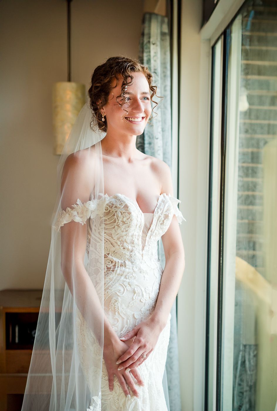 Bridal portraits near large windows showcase intricate lace detailing on a wedding gown.