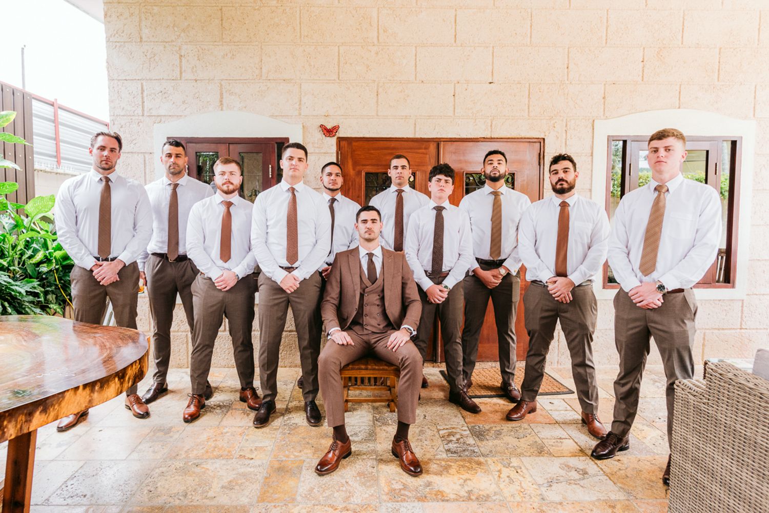 Row of groomsmen showing off their brown dress shoes and socks while seated on church steps for a wedding photo.