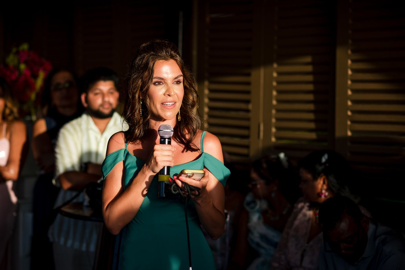 Wedding speaker in teal dress addressing guests during evening reception.
