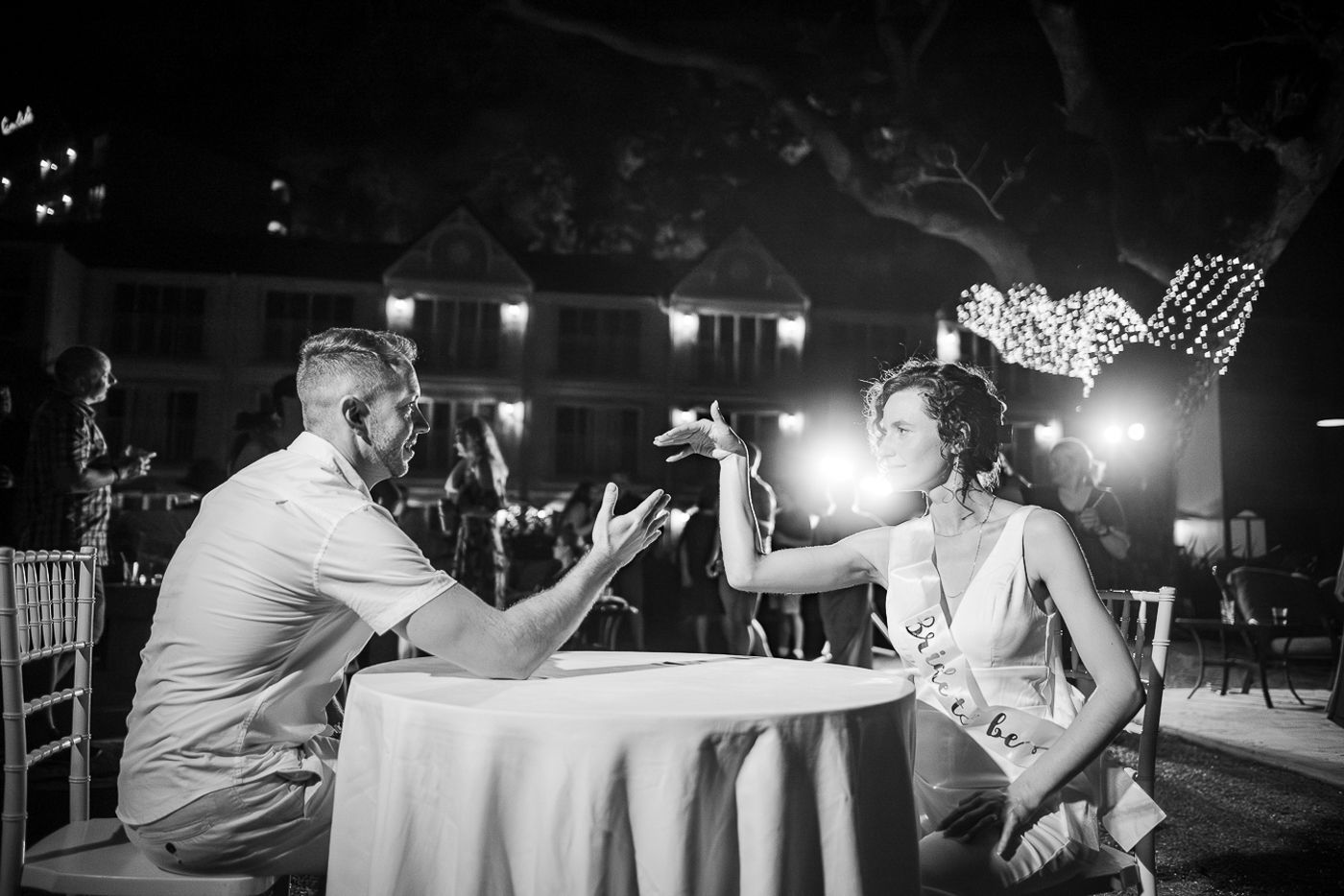 A black and white photo of two people arm wrestling at a candlelit table during an evening event.