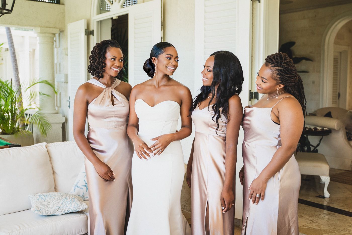 Bridal party in blush pink dresses shares a joyful moment on an elegant white couch.